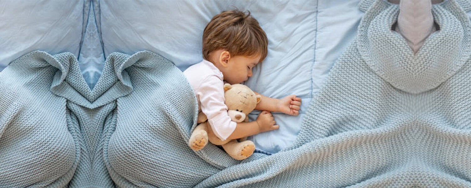 小孩抱著熊娃娃睡在藍色床單上