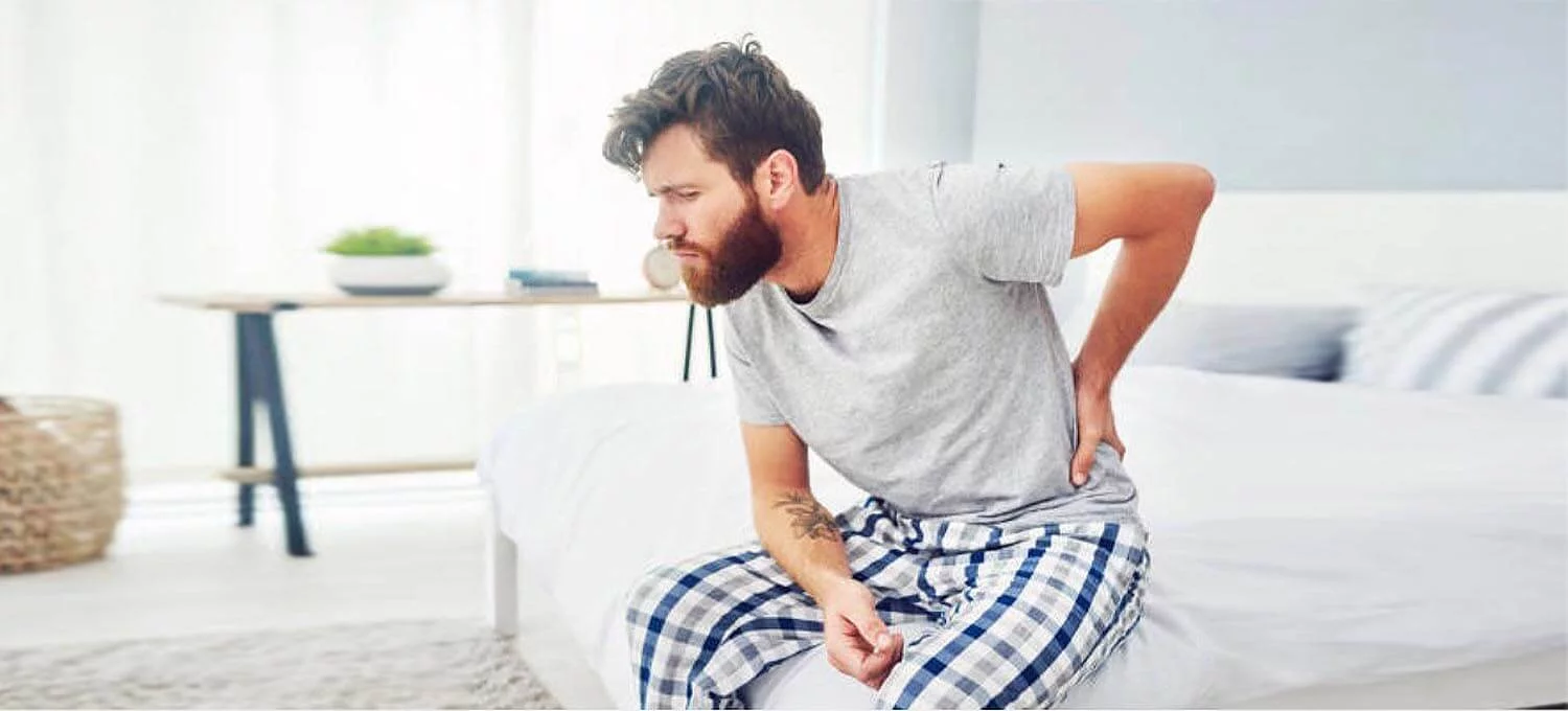 男人坐在床邊覺得腰痛手扶著腰